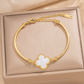 A gold-plated bangle bracelet with a white mother-of-pearl four-leaf clover charm.