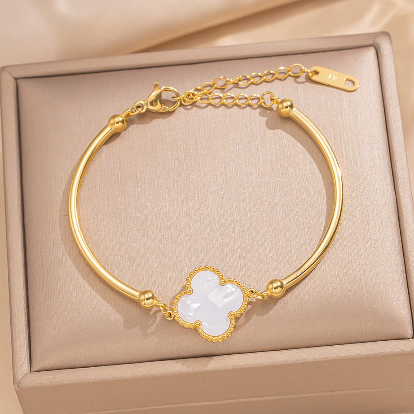 A gold-plated bangle bracelet with a white mother-of-pearl four-leaf clover charm.